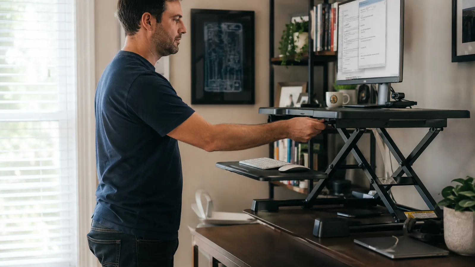 Person adjusting the height of a desk converter at their home office workstation