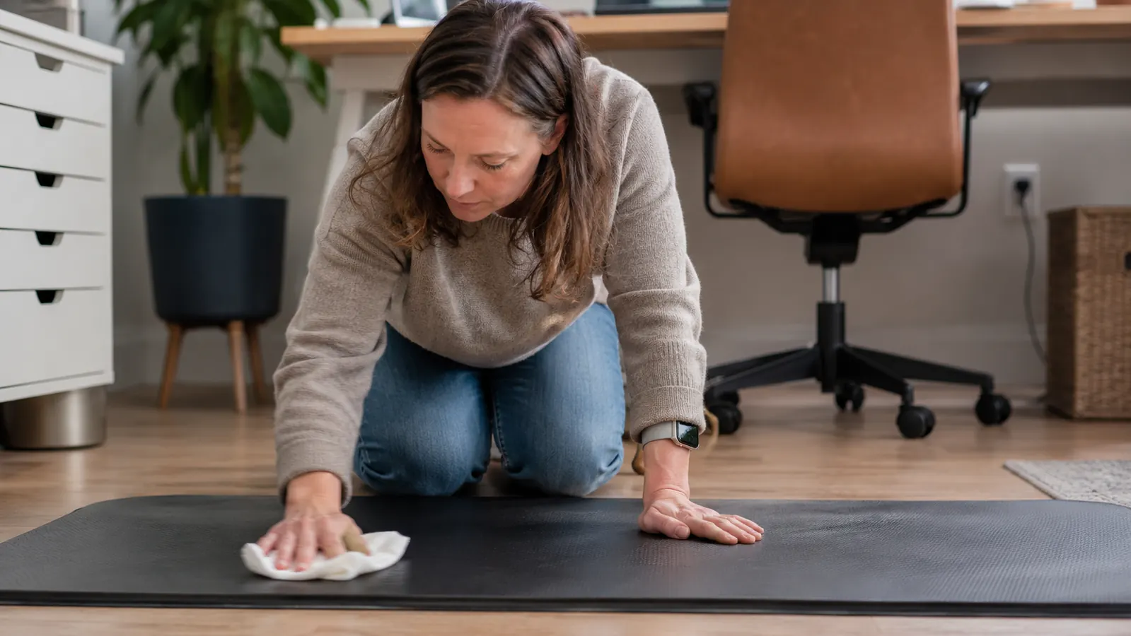 Person wiping down a black foam mat with a damp cloth in a home office