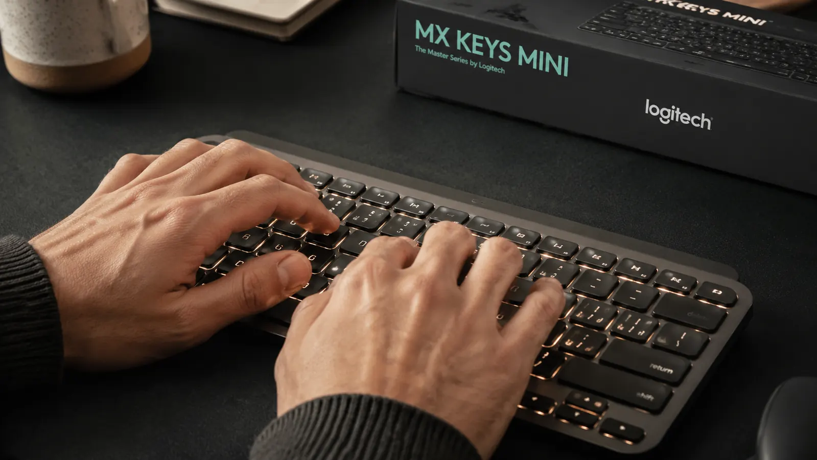 Hands typing on the Logitech MX Keys Mini keyboard at a home office desk