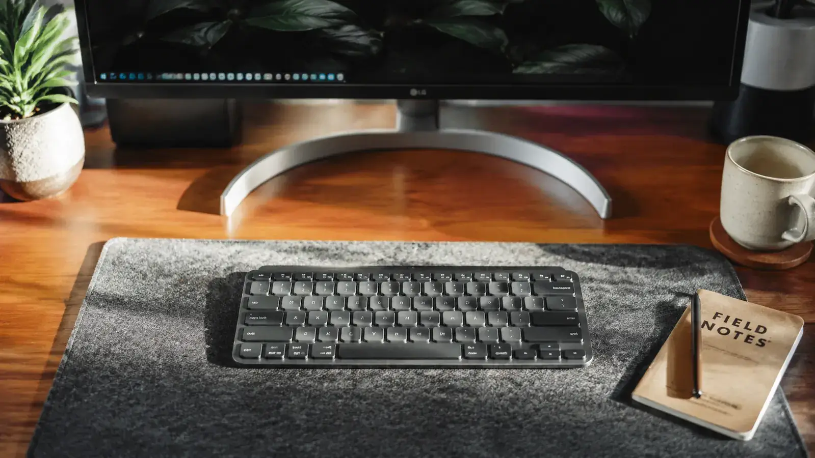 Home office desk with a compact keyboard, monitor, and notebook in a tidy workspace