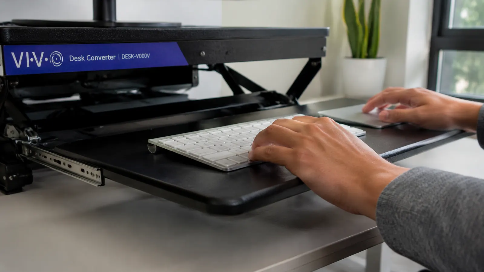 Underside view of the VIVO desk converter showing keyboard tray fully extended and lowered beneath the main platform